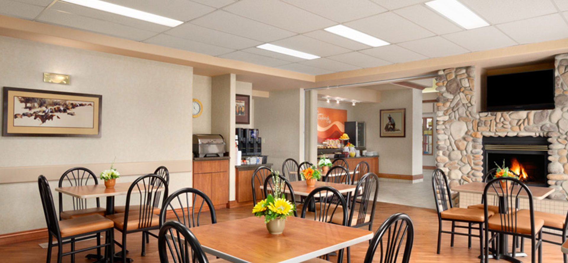 Large view of a bright breakfast room with stone fireplace, tables, chairs and fresh flowers at Days Inn Red Deer, Alberta.
