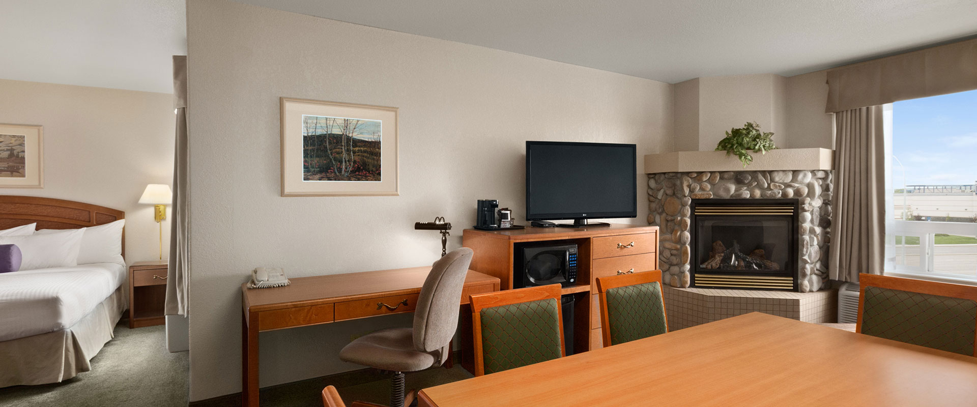 Large view of a one bed suite with workspace, office chair, TV, microwave and stone fireplace at Days Inn Red Deer, Alberta.
