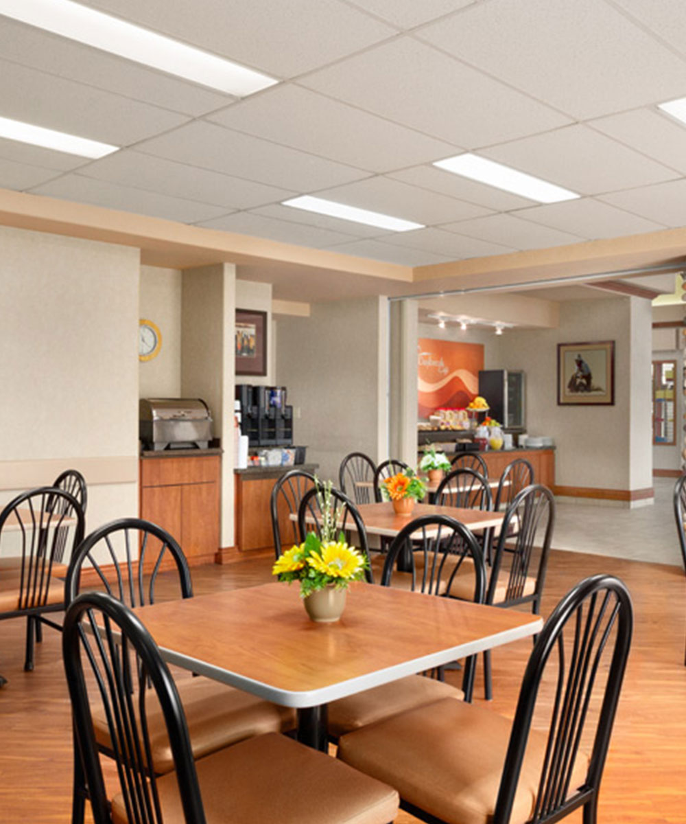 The breakfast room at Days Inn Red Deer, Alberta with coffee kiosk, breakfast counter and eating table with chairs and flowers.
